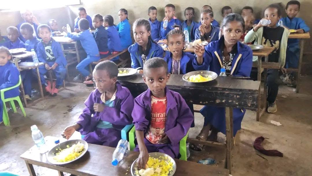 Children seated at desks with plates of food
