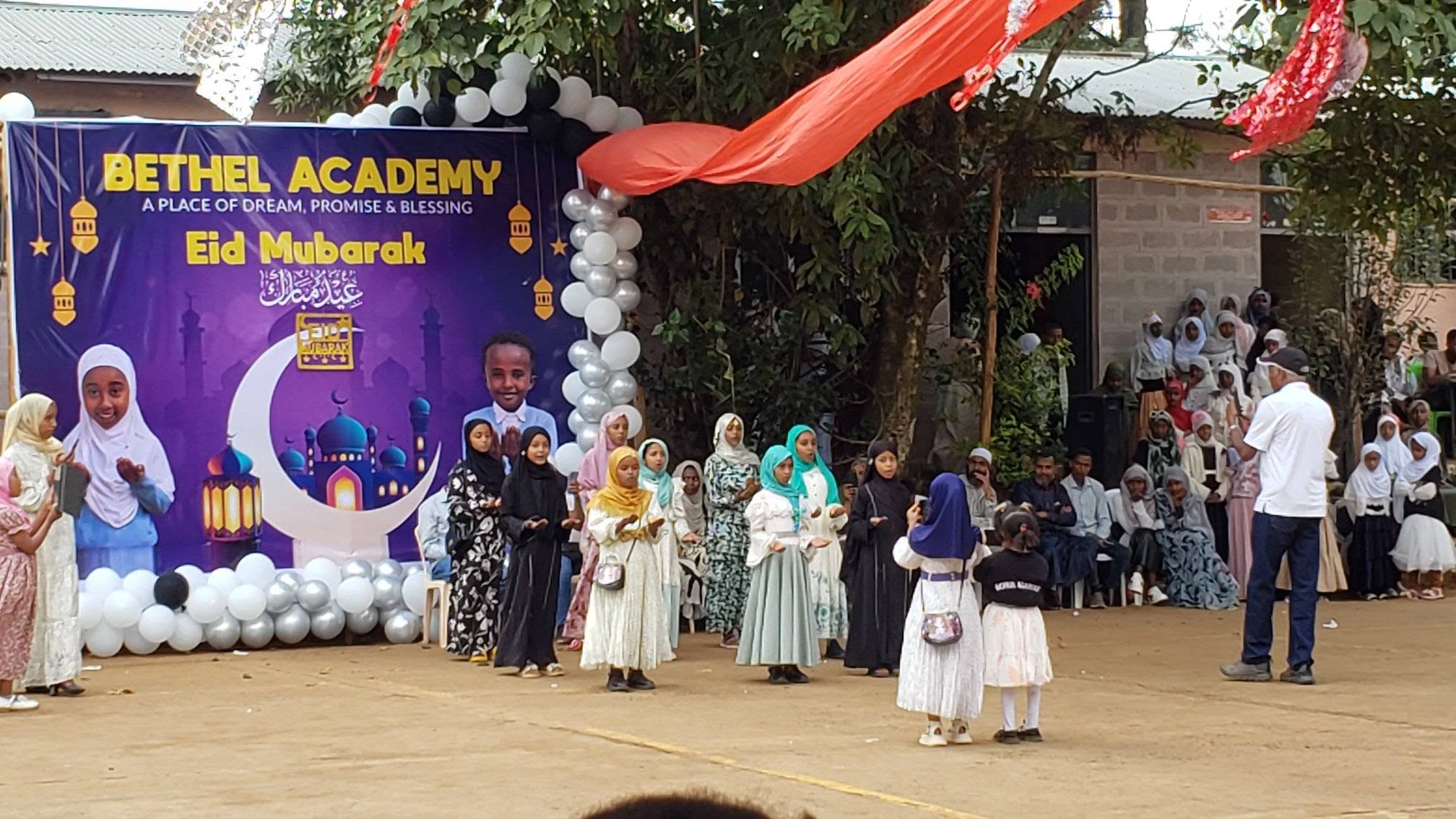 Children performing in front of the Bethel Academy Eid banner