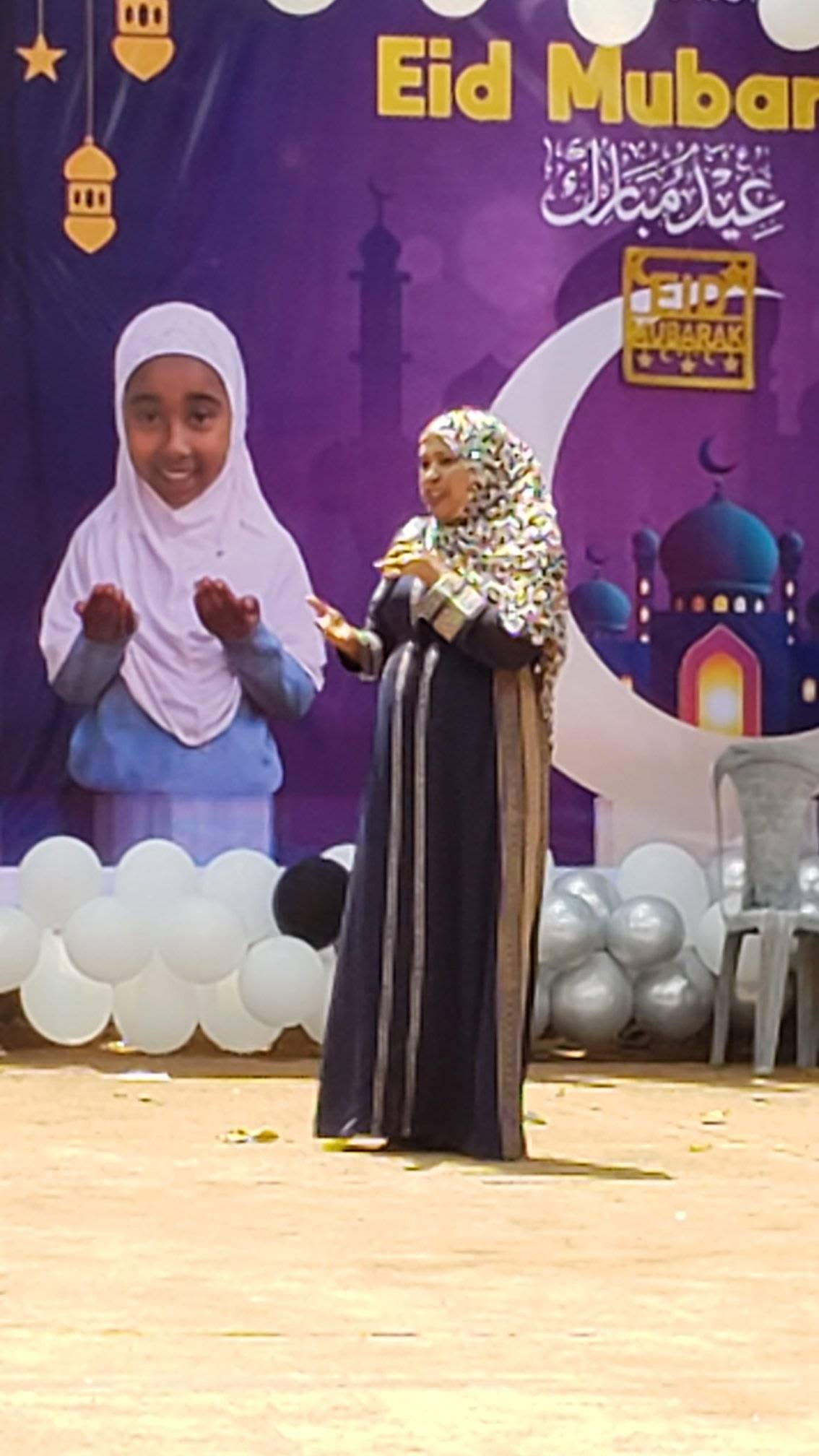 Children with a microphone in front of Eid decorations