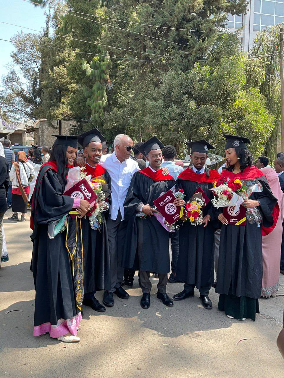 Graduates in academic gowns gathered with flowers outdoors