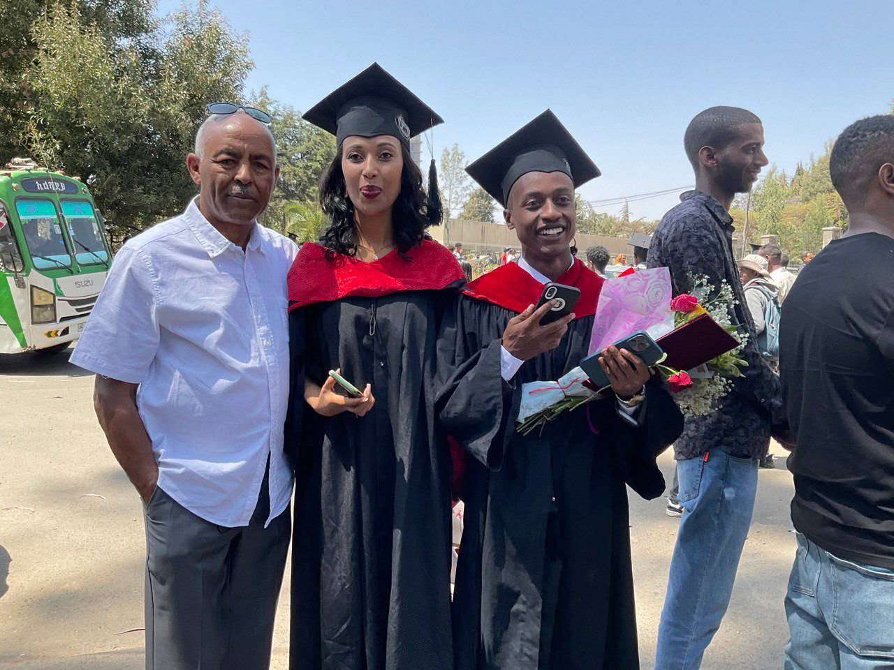 Graduates with flowers posing with an adult at graduation