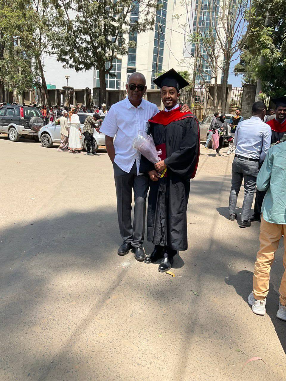 A graduate in academic gown standing with an adult outdoors