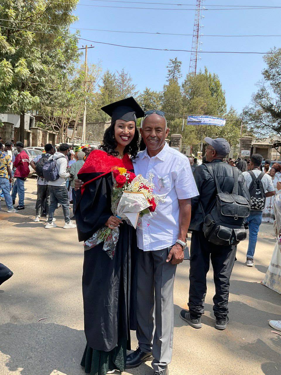 A graduate holding flowers posing with an adult
