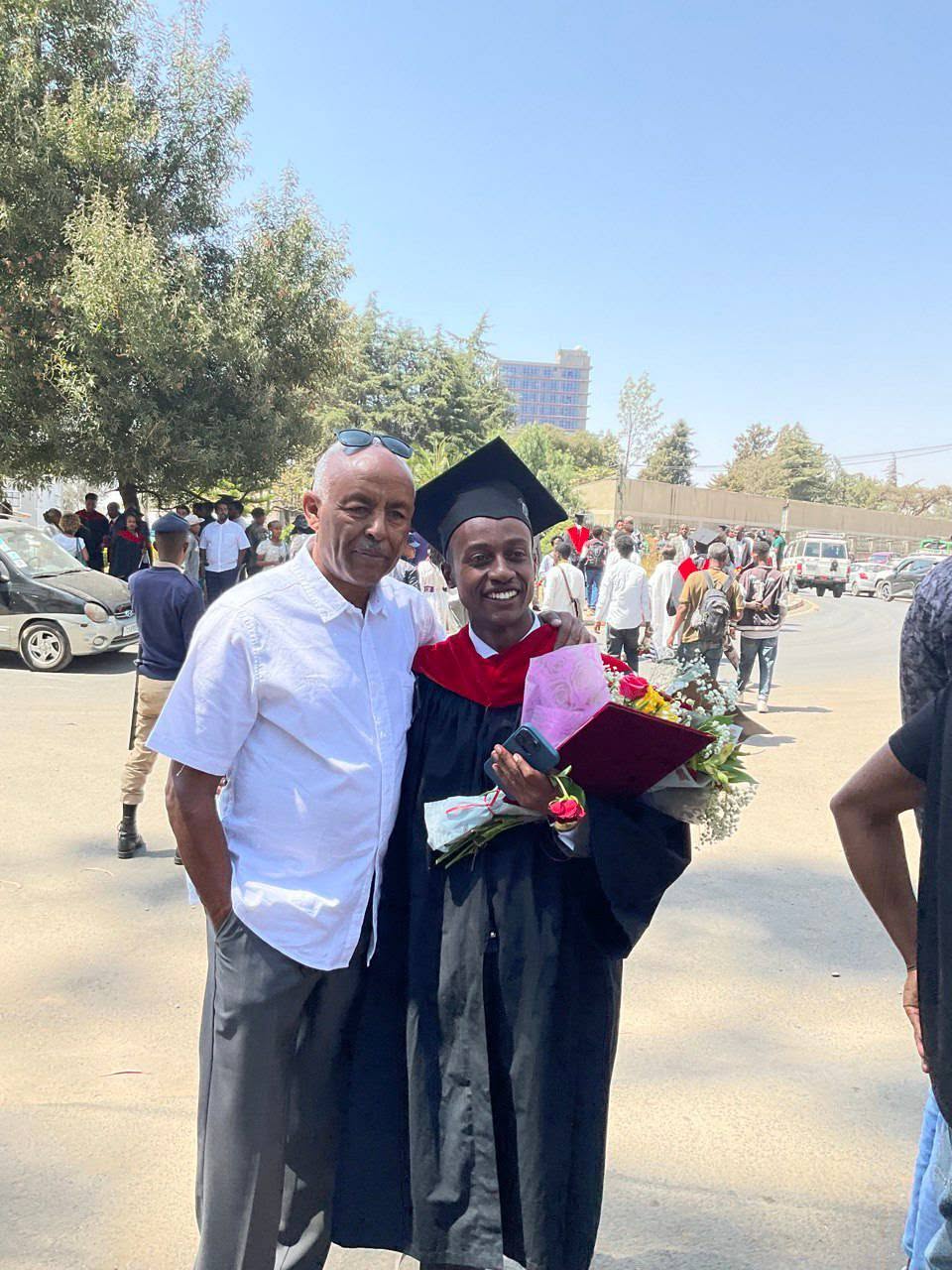 A graduate holding flowers beside an adult